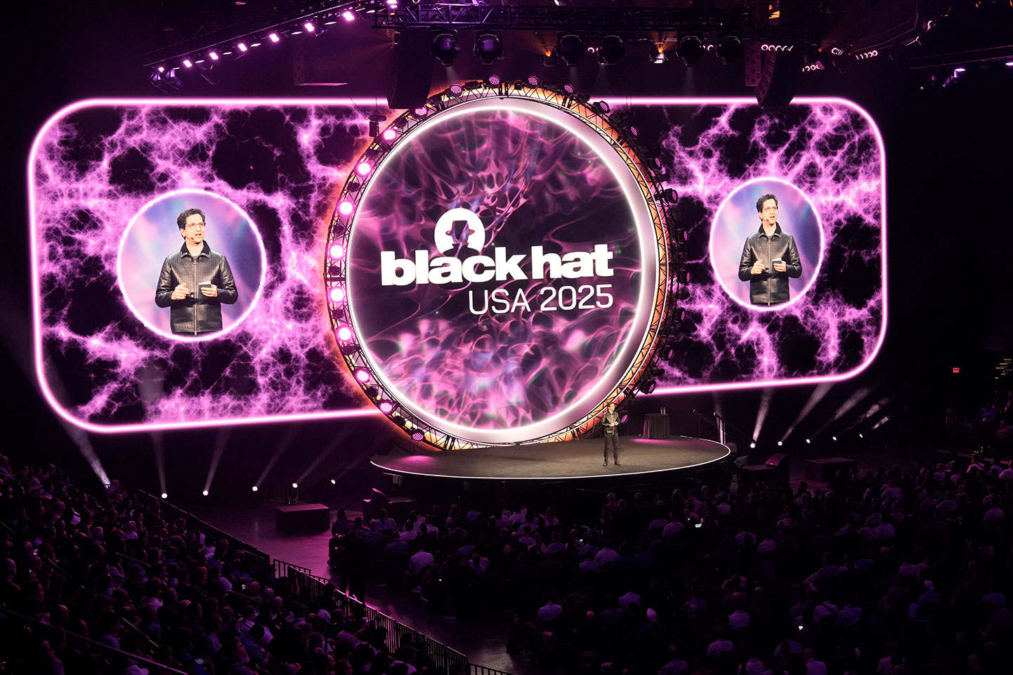 Black Hat founder Jeff Moss stands on stage in front of the Black Hat logo and addresses a crowd at Black Hat USA 2025.
