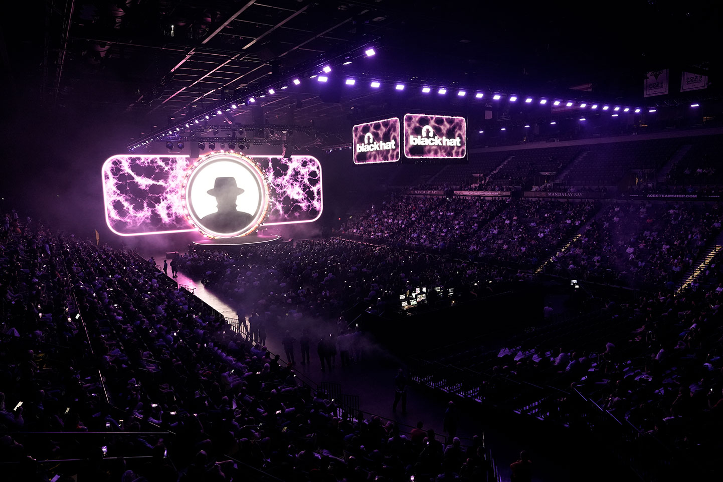 Aerial photo shows an arena-type space filled with people, while the Black Hat logo appears on suspended screens as well as behind the stage, at Black Hat USA 2025.